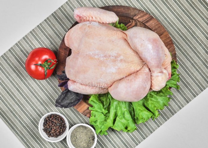 Raw whole chicken on wooden plate with lettuce, tomato and spices. High quality photo